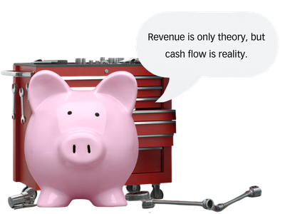 A pink piggy bank standing in front of a red tool box and miscellaneous parts scattered on the ground, with a speech bubble that says 'Revenue is only theory, but cash flow is reality.'.